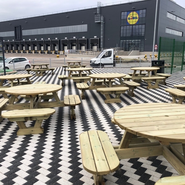 Round pub style picnic benches with rounded seats and umbrella holes in commercial outdoors venue near warehouse