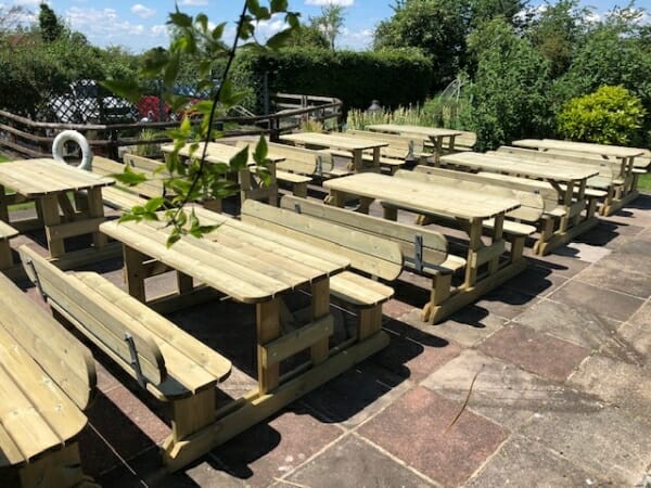 Multiple wooden picnic benches with rounded edges and seat backs in hospitality venue outdoor seating area